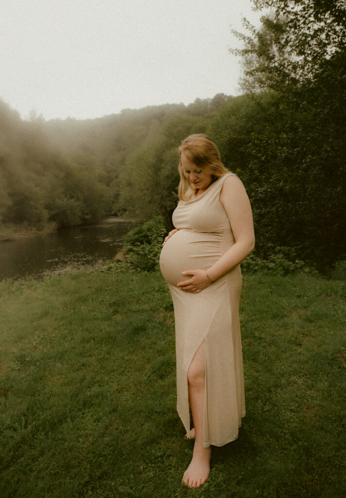 Schwangere im beigen Kleid auf einer Wiese am Wald