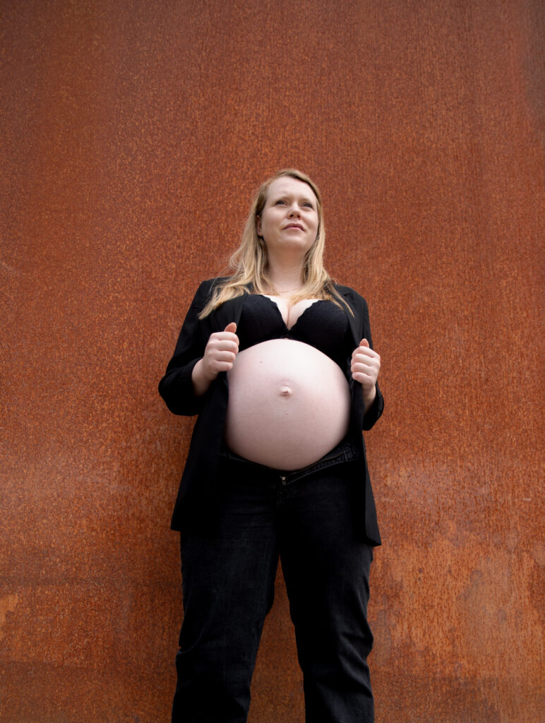 Schwangere hält ihren Bauch vor rostroter Wand