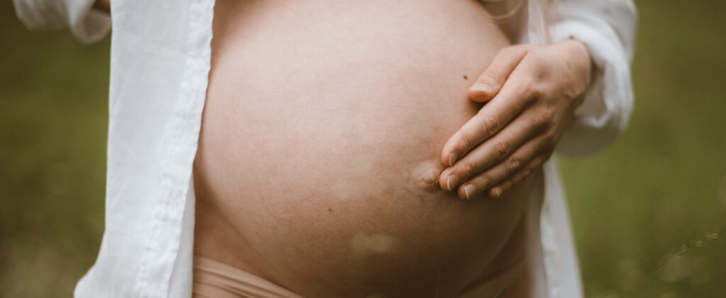 Hände auf einem Babybauch unter weißer Bluse