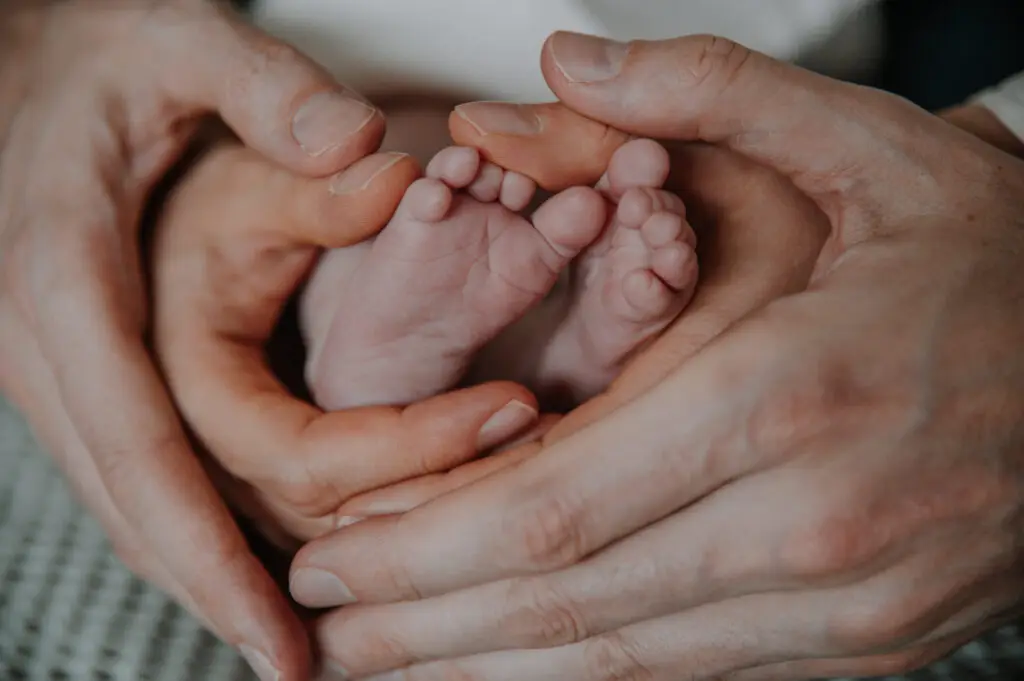 Elternhände formen ein Herz um die Füße ihres Babys