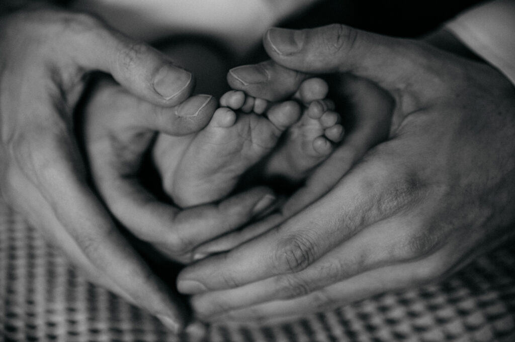 Elternhände formen ein Herz um Babyfüße, Schwarz-Weiß